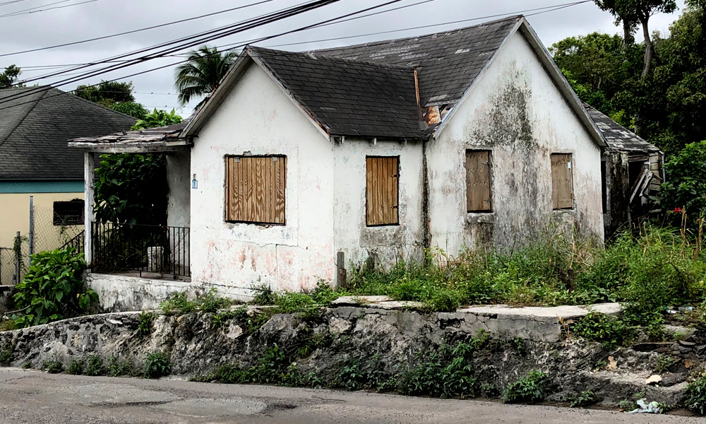 Another filthy, boarded-up home/business alongside a crumbled wall and street, inland Bahamas.