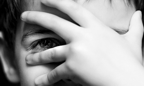 boy covering face with hand one eye peeking